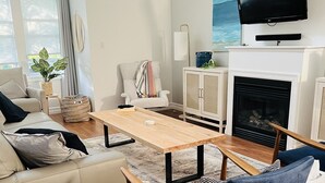 Un salon moderne comprenant un canapé, une table basse, un fauteuil bleu, une cheminée et un téléviseur fixé au mur.