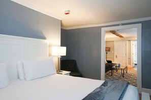 Ein Hotelzimmer mit einem großen Bett, einem Nachttisch, einer Lampe, einem Sessel und Blick auf den Flur.