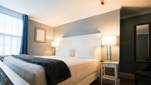 Hotellihuone, jossa on suuri sänky, yöpöydät lamppuineen, tuoli ja seinällä oleva kehystetty taulu.