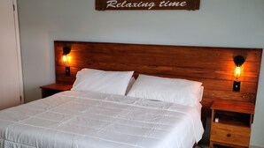 A neatly made bed with a wooden headboard, two bedside tables with lamps, and a 'Relaxing time' sign on the wall.