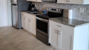 A modern kitchen with white cabinets, stainless steel appliances, a granite countertop, and a herringbone-patterned backsplash.