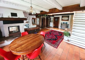 Amplia sala de estar con una mesa de comedor de madera y sillas rojas, una chimenea y un tapete rojo estampado.
