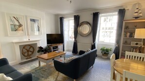 Una sala de estar con sofá, televisor, mesa de madera y mesa de comedor con sillas.