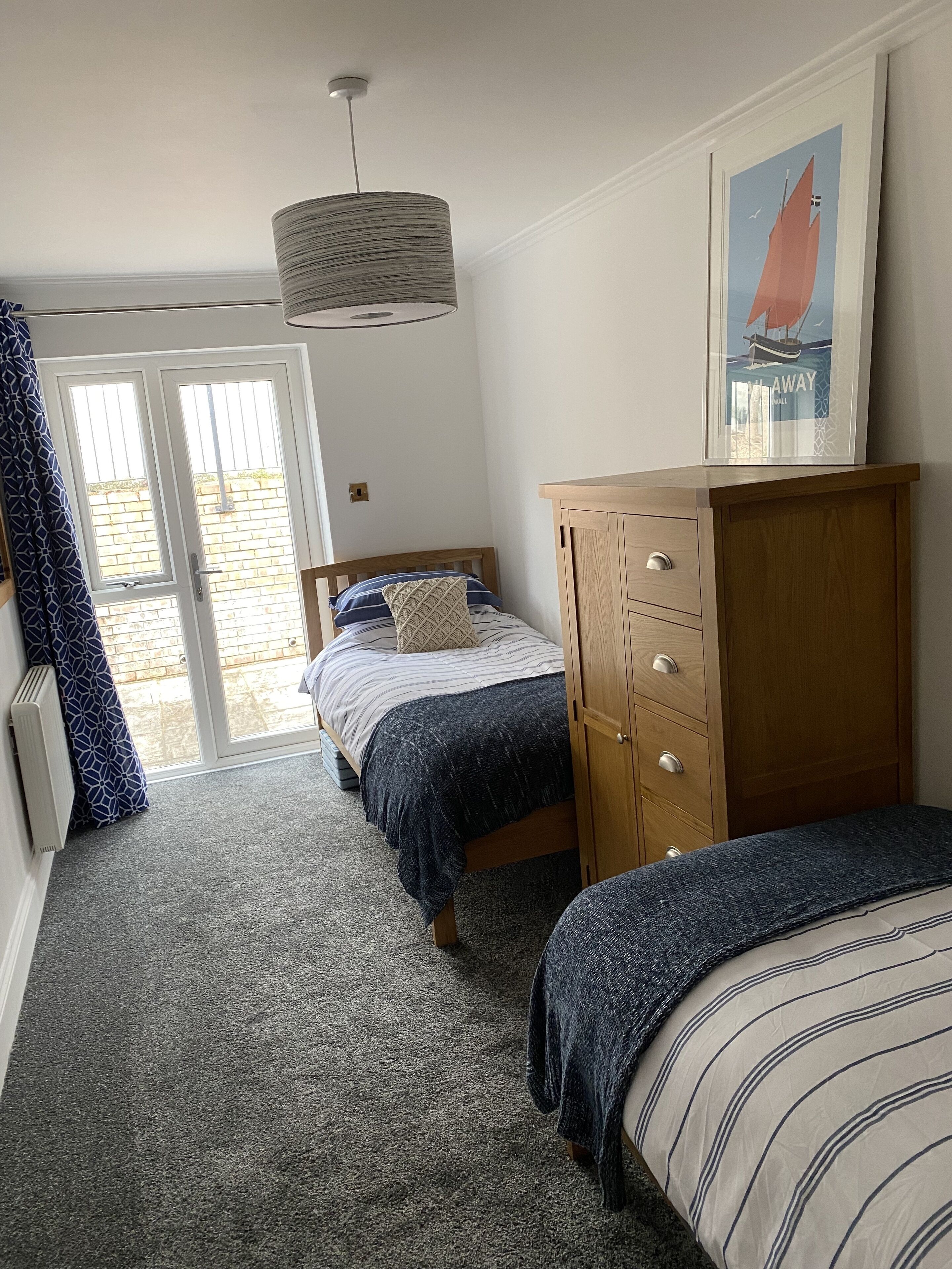 Una camera da letto con due letti singoli, un comò in legno, una lampada a sospensione e un quadro appeso al muro.
