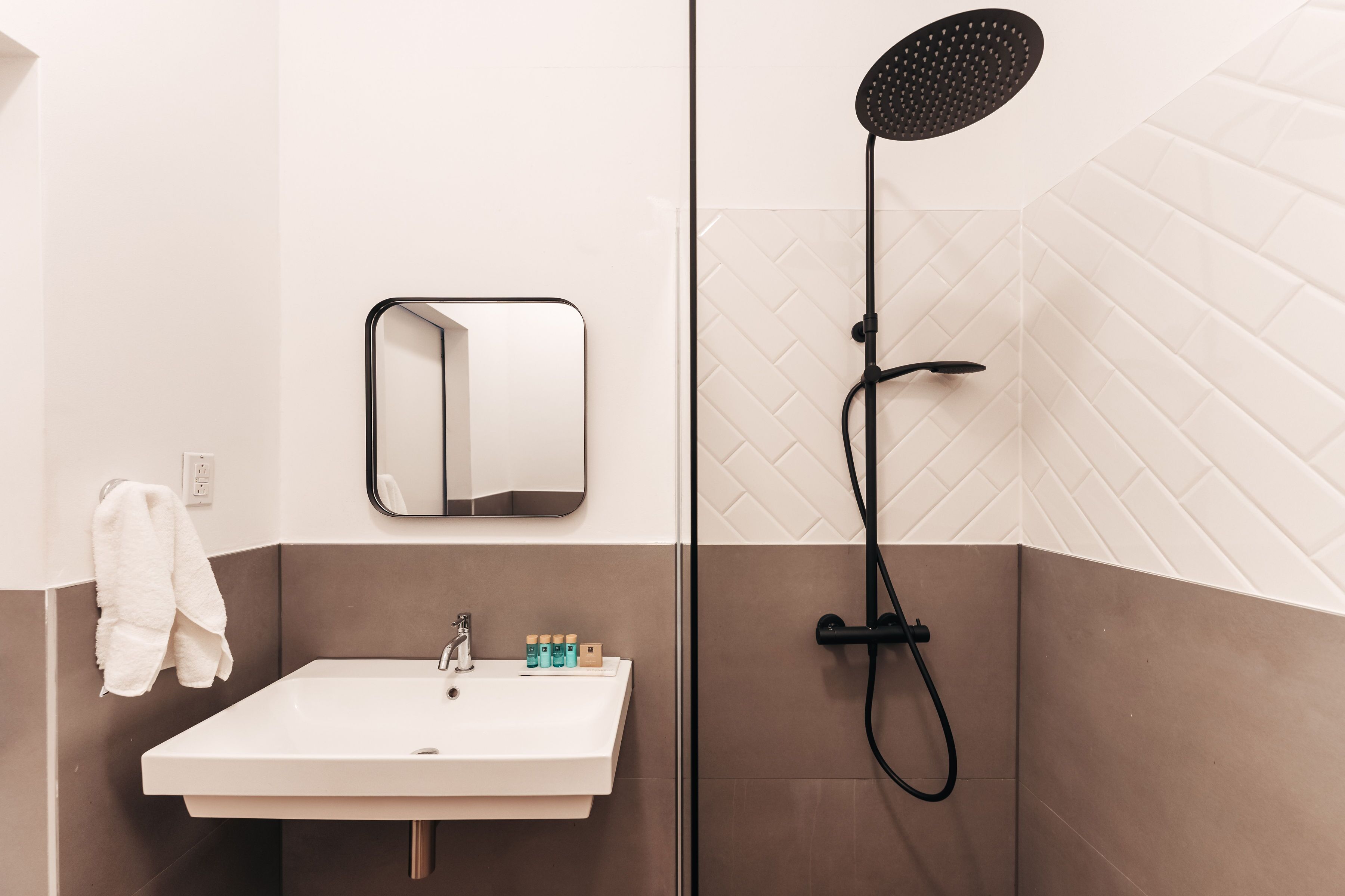 Un bagno con un lavandino bianco, uno specchio e una doccia con un tubo nero.