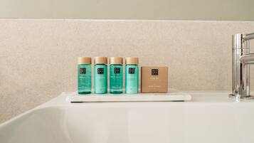 A bathroom sink with a white countertop and a chrome faucet. On the countertop, there are four bottles of body care products and a brown box labeled "RITUAL OF KARMA".