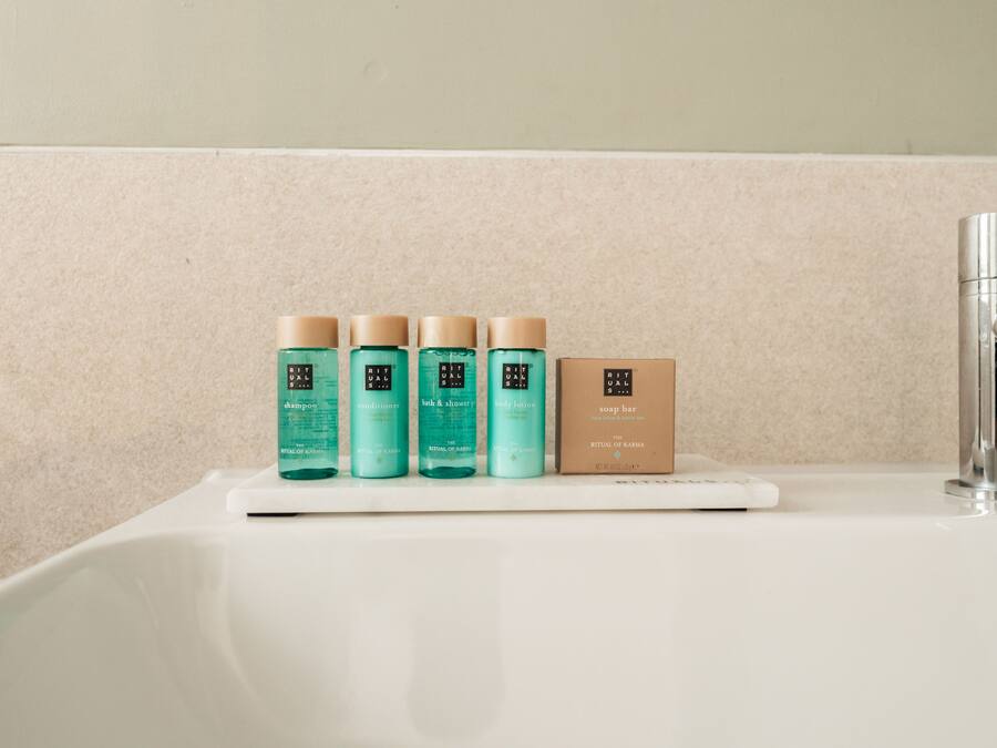 A bathroom sink with a white countertop and a chrome faucet. On the countertop, there are four bottles of body care products and a brown box labeled "RITUAL OF KARMA".