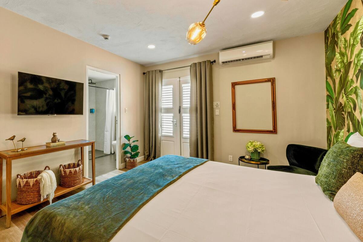Une chambre d’hôtel comprenant un lit, une console en bois avec des paniers, un téléviseur, un appareil de climatisation et un grand miroir.