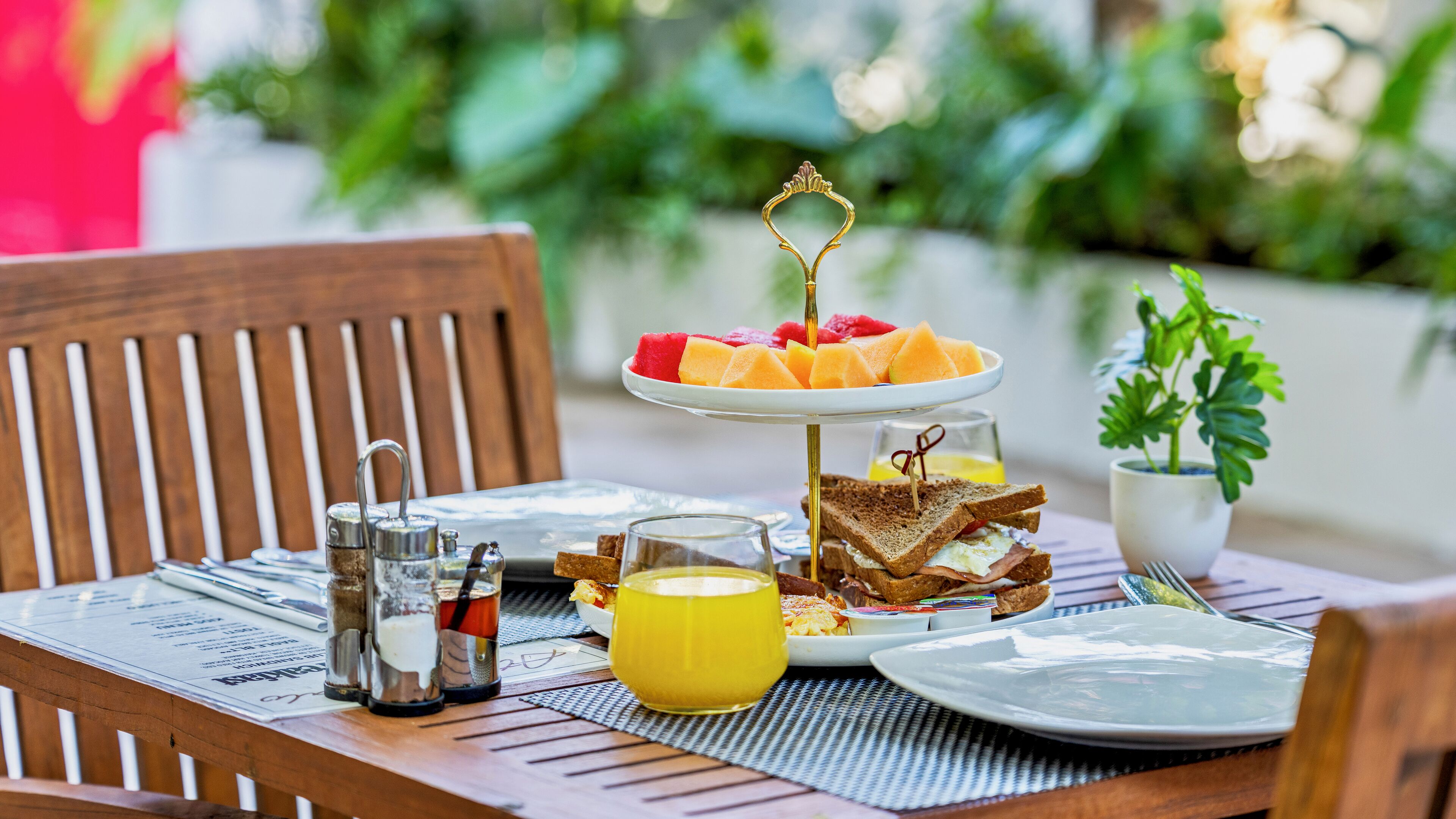 Mesa de madeira com torradas, um copo de sumo de laranja e um prato de fruta.