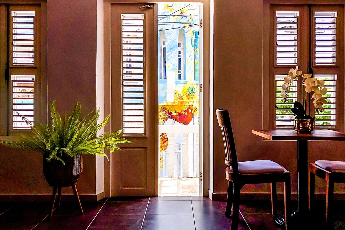 Une pièce comprenant une table à manger, deux chaises, une plante en pot et une vue sur l’extérieur, visible à travers une porte dotée d’une fenêtre.