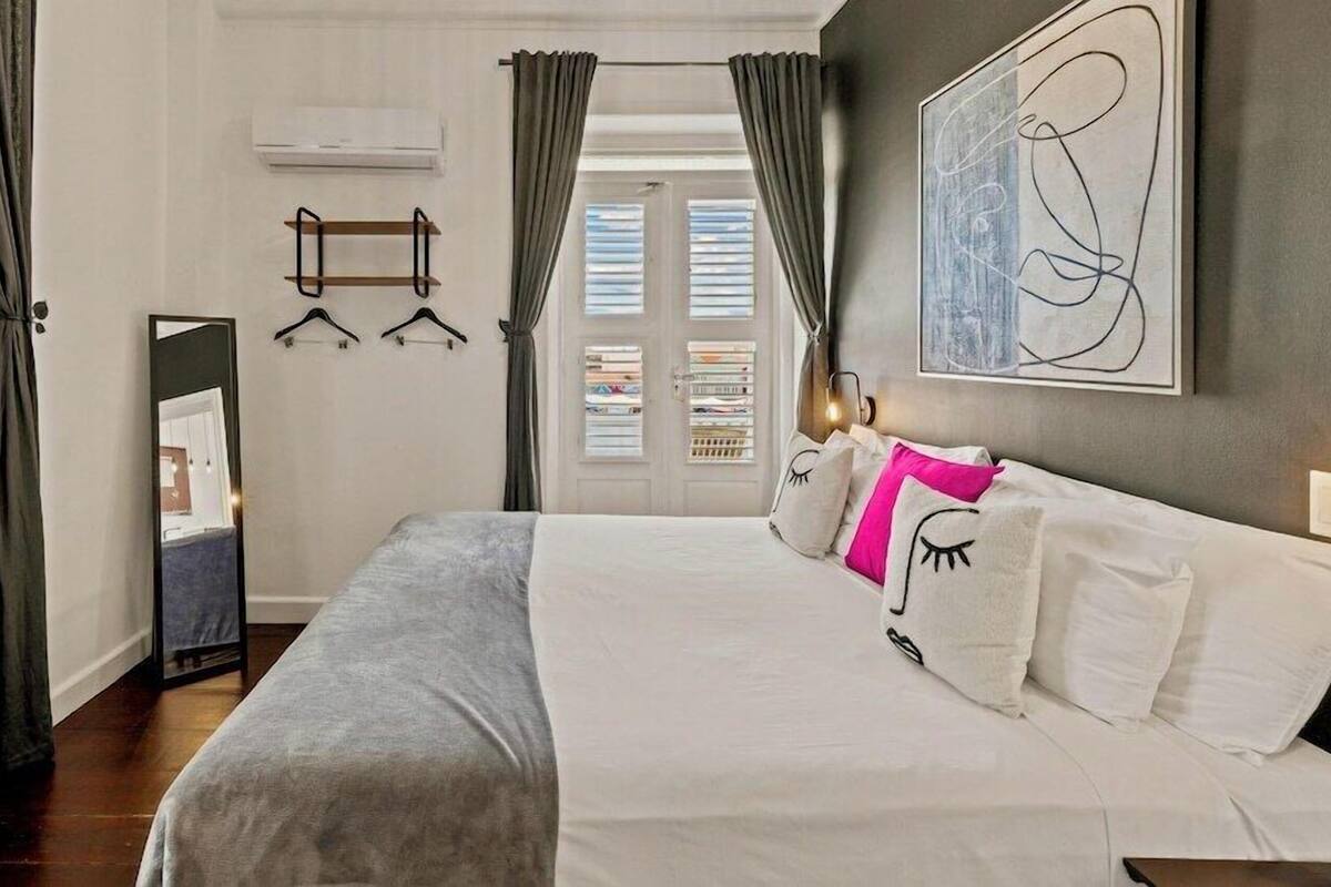 Une chambre à coucher avec un lit, un miroir, une armoire et une porte avec des rideaux.