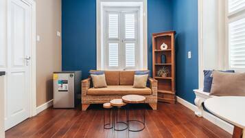 Een kamer met een blauwe muur, een witte deur, een houten kast, een bank, een klein tafeltje en een koelkast.