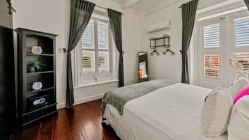Quarto de hotel com cama, guarda-roupa, espelho e janela com persianas.