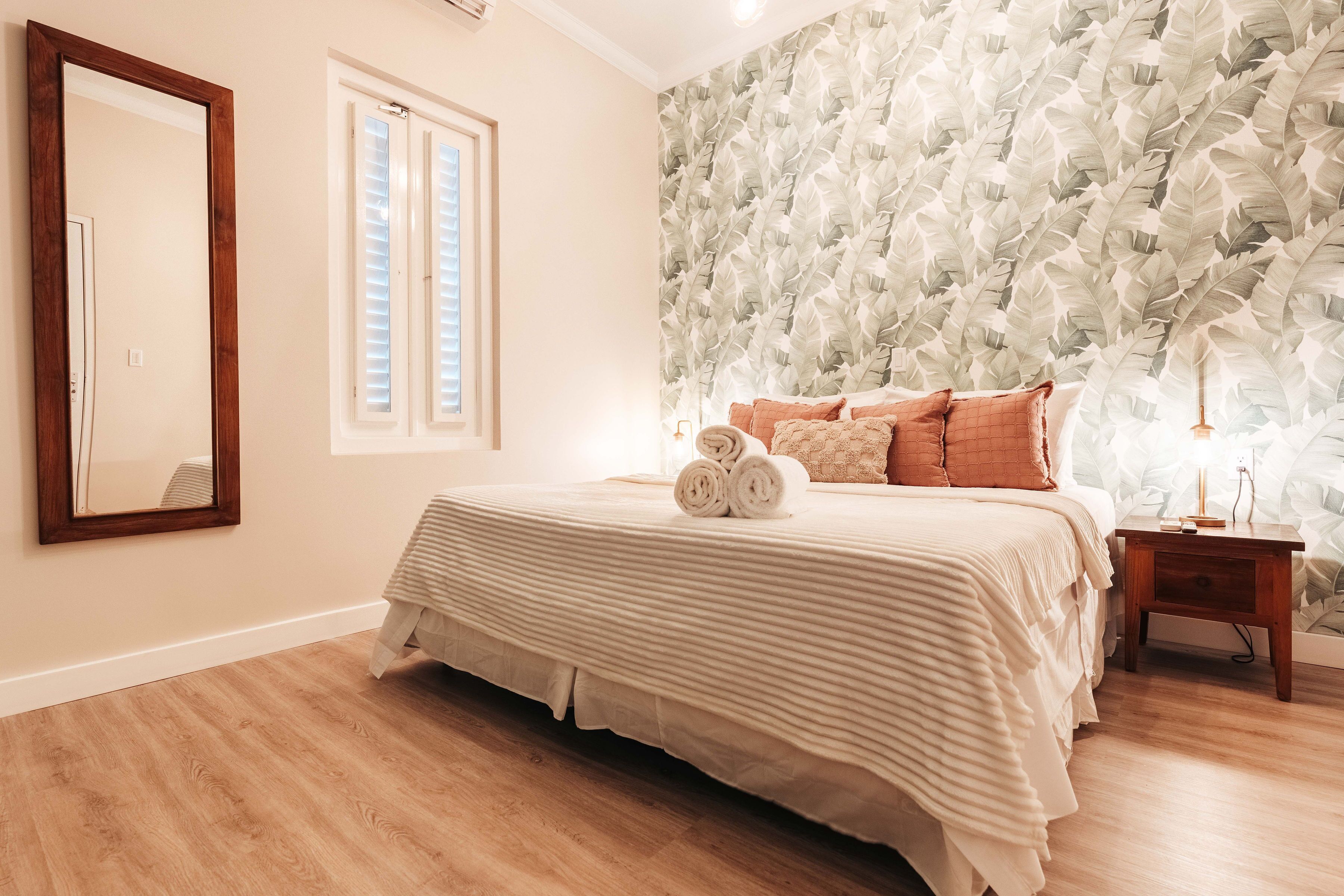 Un dormitorio con una cama grande, una mesita de noche de madera, un espejo y una ventana con persianas.
