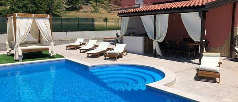A swimming pool with sun loungers and a covered seating area.