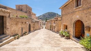 Une rue étroite bordée d’immeubles en pierre, dotés de portes et de fenêtres en arc de cercle, qui mène vers une colline au loin.