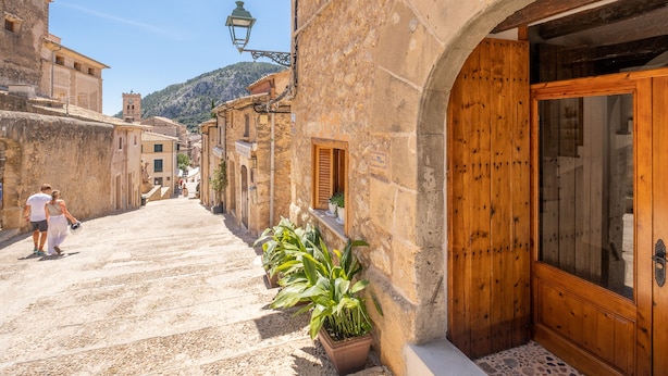 Une rue étroite bordée d’immeubles en pierre, avec une porte en bois et un pot de fleurs.