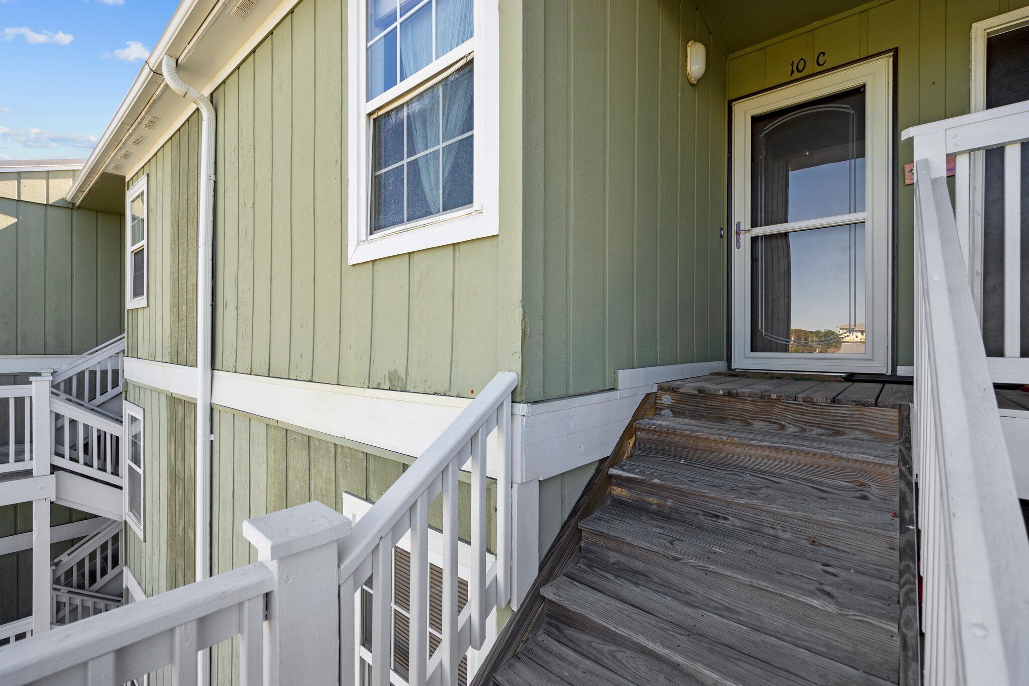 A green building with a white staircase leading to a door marked "10 C".