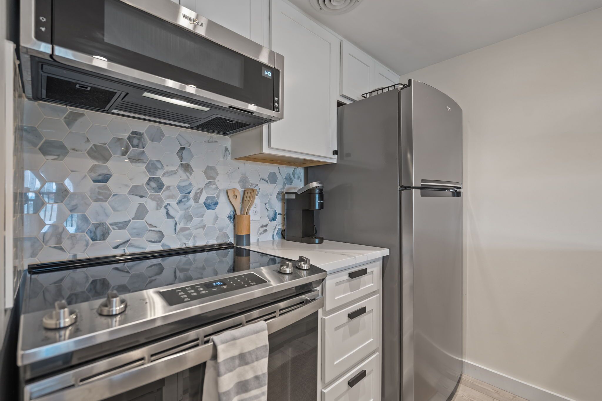 A modern kitchen with a stainless steel stove, oven, and refrigerator, white cabinets, and a hexagonal tile backsplash.