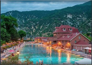 A swimming pool area with multiple pools, a building with a red roof, and a mountainous backdrop.
