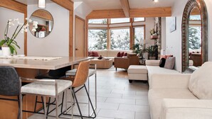 A spacious living area with a wooden ceiling, large windows, a dining table, and a sofa.