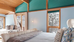 A bedroom with a large bed, a chair, and a window with a view of trees.