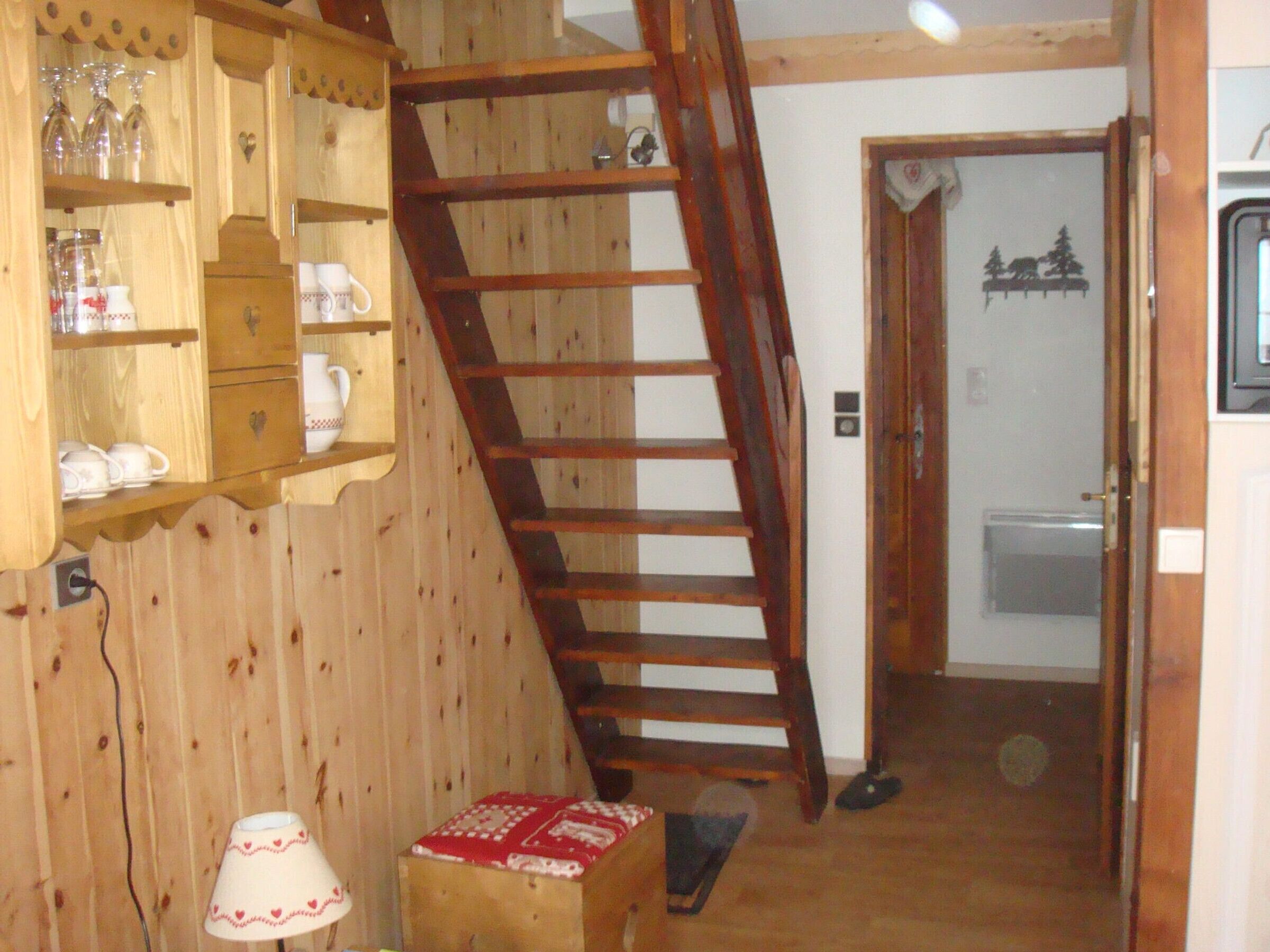 Een houten interieur met een houten trap, een plank met glazen en een kleine tafel met een lamp.