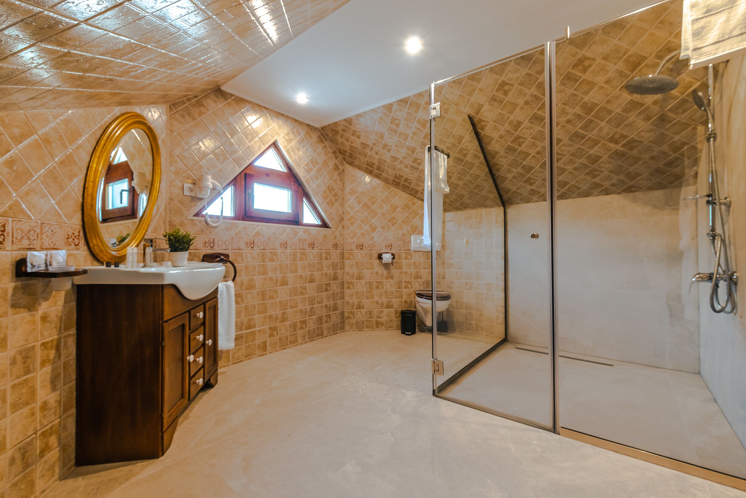 Un baño con ducha de vidrio, tocador con espejo y una ventana pequeña.