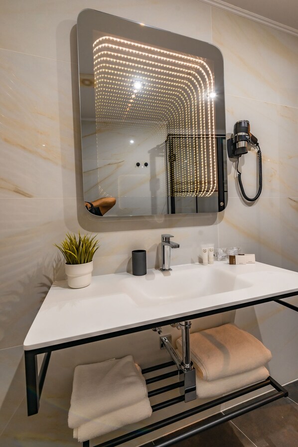 A modern bathroom with a white sink, a large mirror with LED lights, a potted plant, and a towel rack. - Hotel Korona (Sighisoara)
