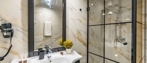 A modern bathroom with a white sink, a large mirror, a handheld showerhead, and a potted plant.