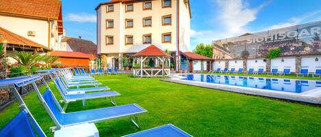 Ein Hotel mit Schwimmbad, Liegestühlen und einer Laube.