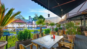 An outdoor patio with a table and chairs, surrounded by potted plants and overlooking a swimming pool area. - Hotel Korona (Sighisoara)