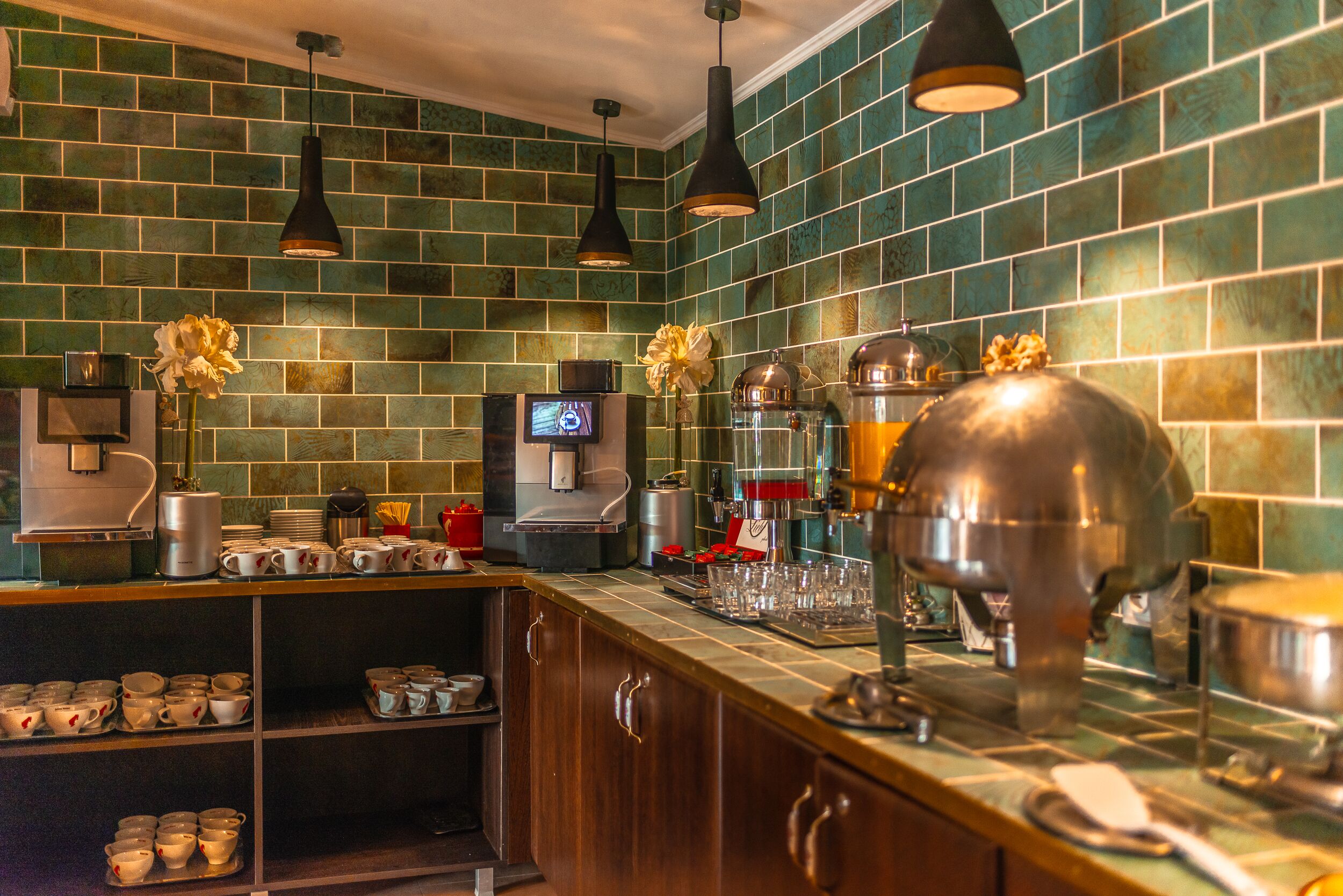 A kitchen with green tiled walls, wooden cabinets, and stainless steel appliances.
