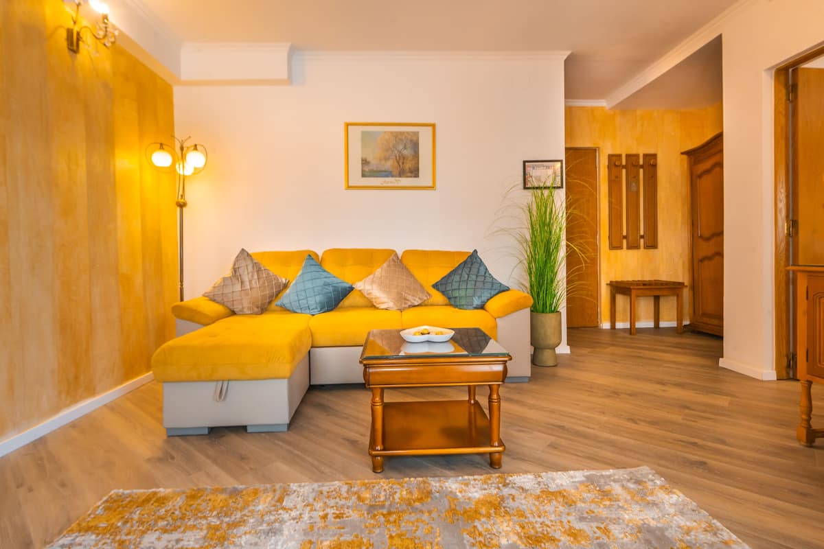 A living room with a yellow sofa, a coffee table, and a painting on the wall.