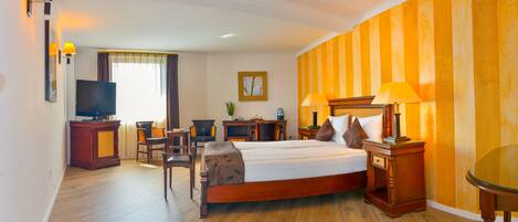 Habitación de hotel con una cama grande, un escritorio con computadora, televisor y ventana con cortinas.