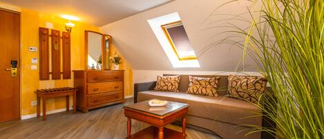 A room with a wooden floor, a sofa with patterned cushions, a wooden side table, a dresser, a mirror, and a skylight.