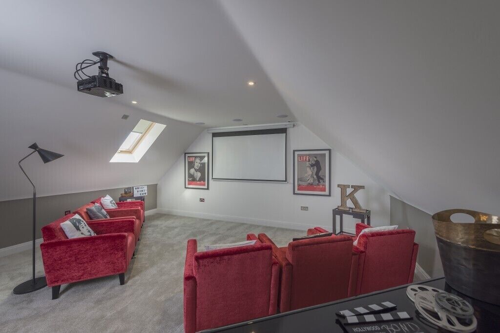 Una sala home theater con poltrone in velluto rosso, un proiettore, uno schermo e poster cinematografici incorniciati.
