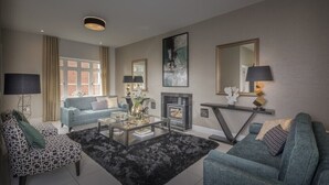 A modern living room with a sofa, armchair, and coffee table, a fireplace, and a large mirror.