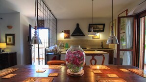 Ett matbord med en vas med blommor, ett kök i bakgrunden och ett fönster med gardiner.