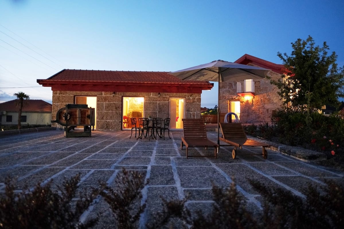 A stone building with a red-tiled roof, outdoor seating, and a barbecue area.