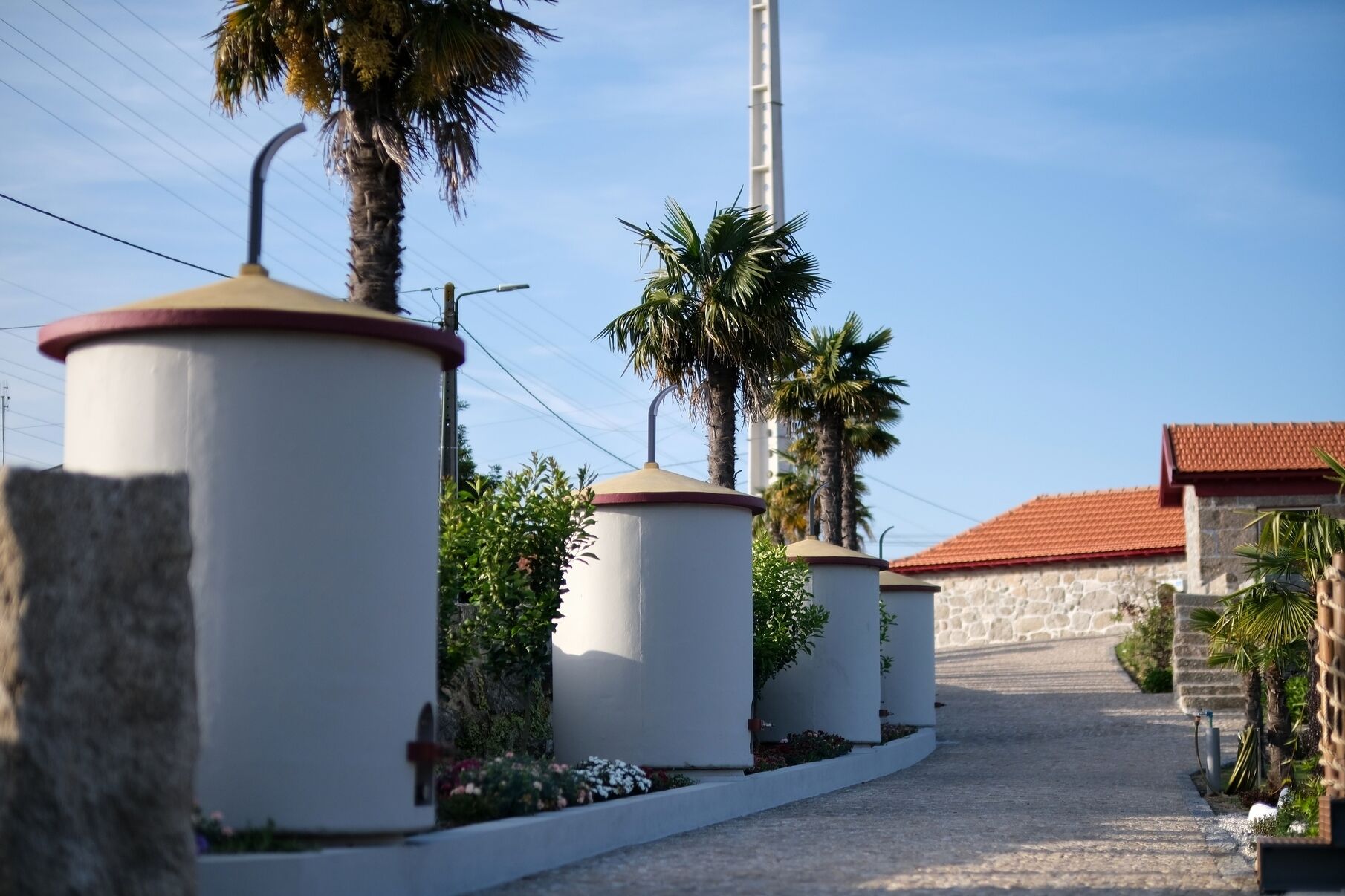 Un sendero bordeado por estructuras cilíndricas blancas, posiblemente tanques de agua, que conduce a un edificio con tejado de tejas rojas.