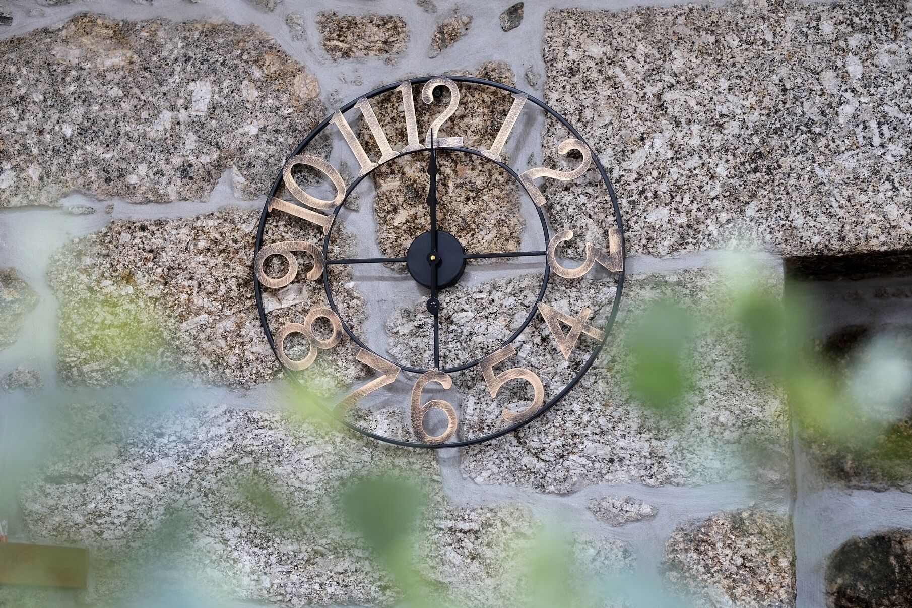 A wall-mounted clock with Roman numerals indicating the hours, set against a stone wall.