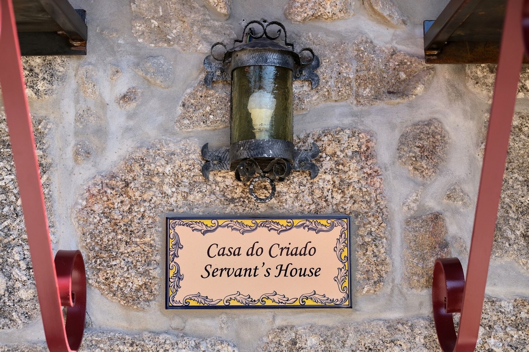 Un muro de piedra con un letrero que dice "Casa do Criado Servant's House" y un farol colgando sobre él.