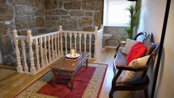 Una sala de estar acogedora con una pared de piedra, un banco de madera, un tapete rojo y un sofá de madera con cojines.
