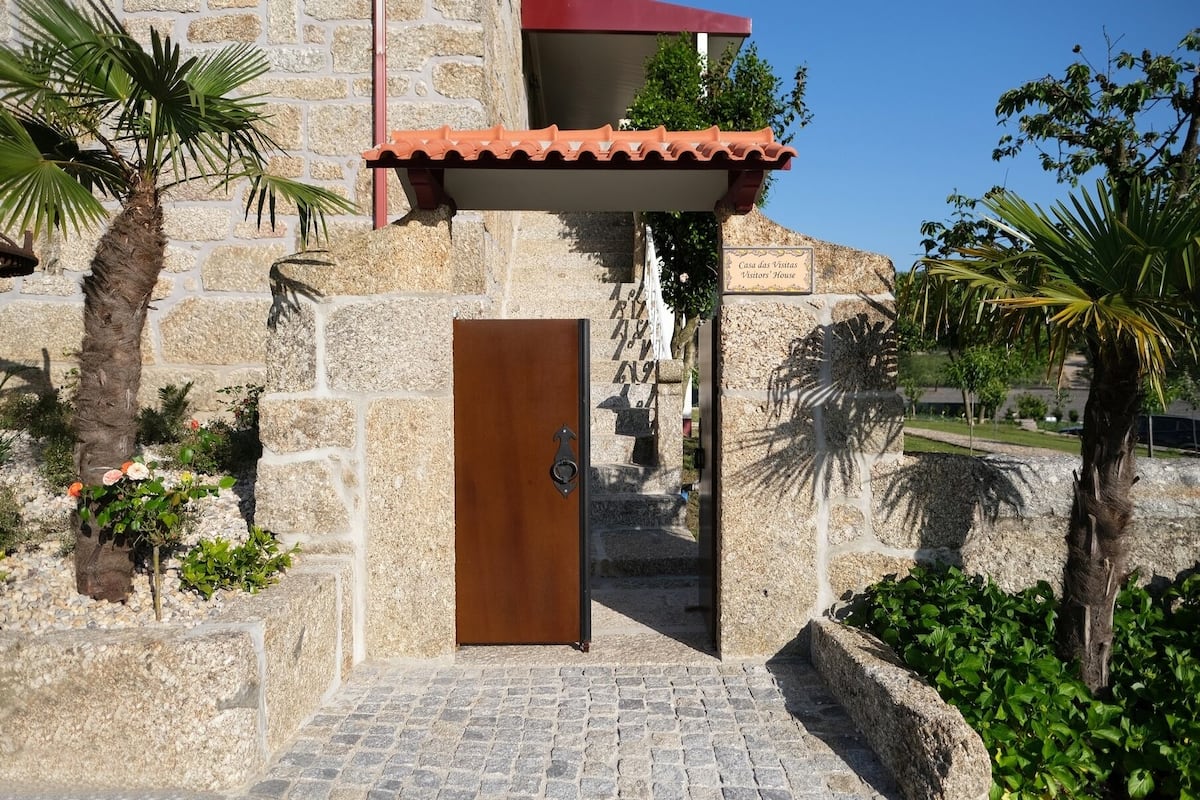 A stone building with a wooden door, a tiled roof, and a sign reading "Casa das Vistas Visitors' House".