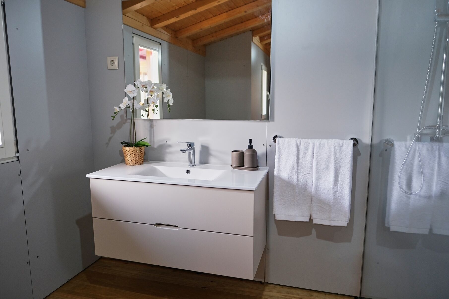 A bathroom with a white sink, a mirror, a towel rack, and a wooden ceiling.