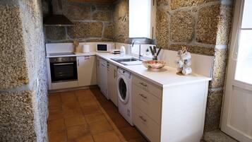 Una cocina compacta con paredes de piedra, horno integrado, lavadora y lavamanos.