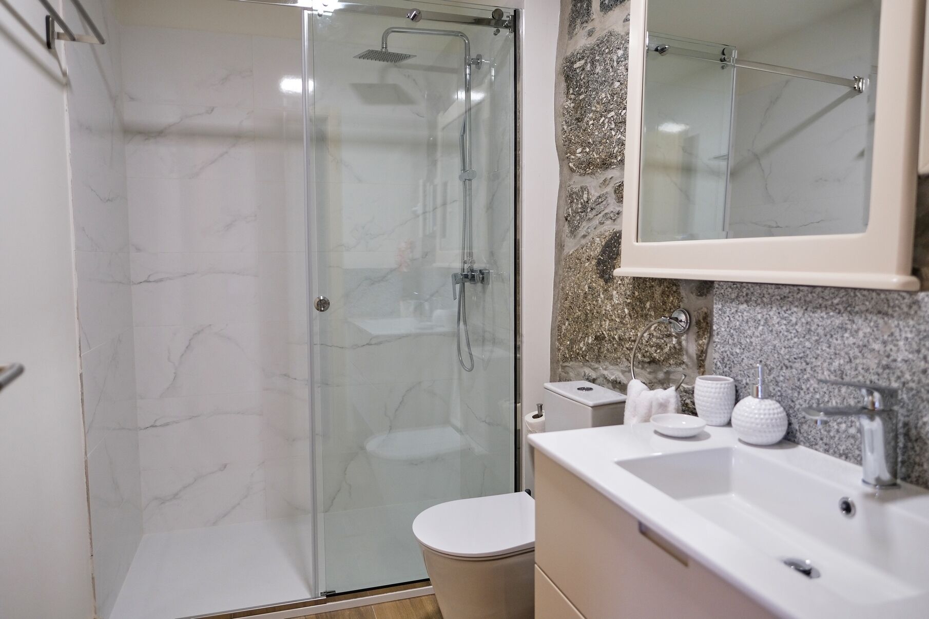 A modern bathroom with a glass-enclosed shower, a toilet, and a sink with a marble countertop.