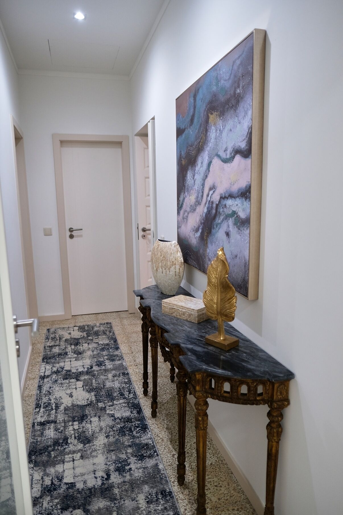 A hallway with a dark marble bench, a gold decorative piece, and a large abstract painting on the wall.