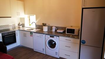 A compact kitchen with a washing machine, microwave, and a refrigerator.